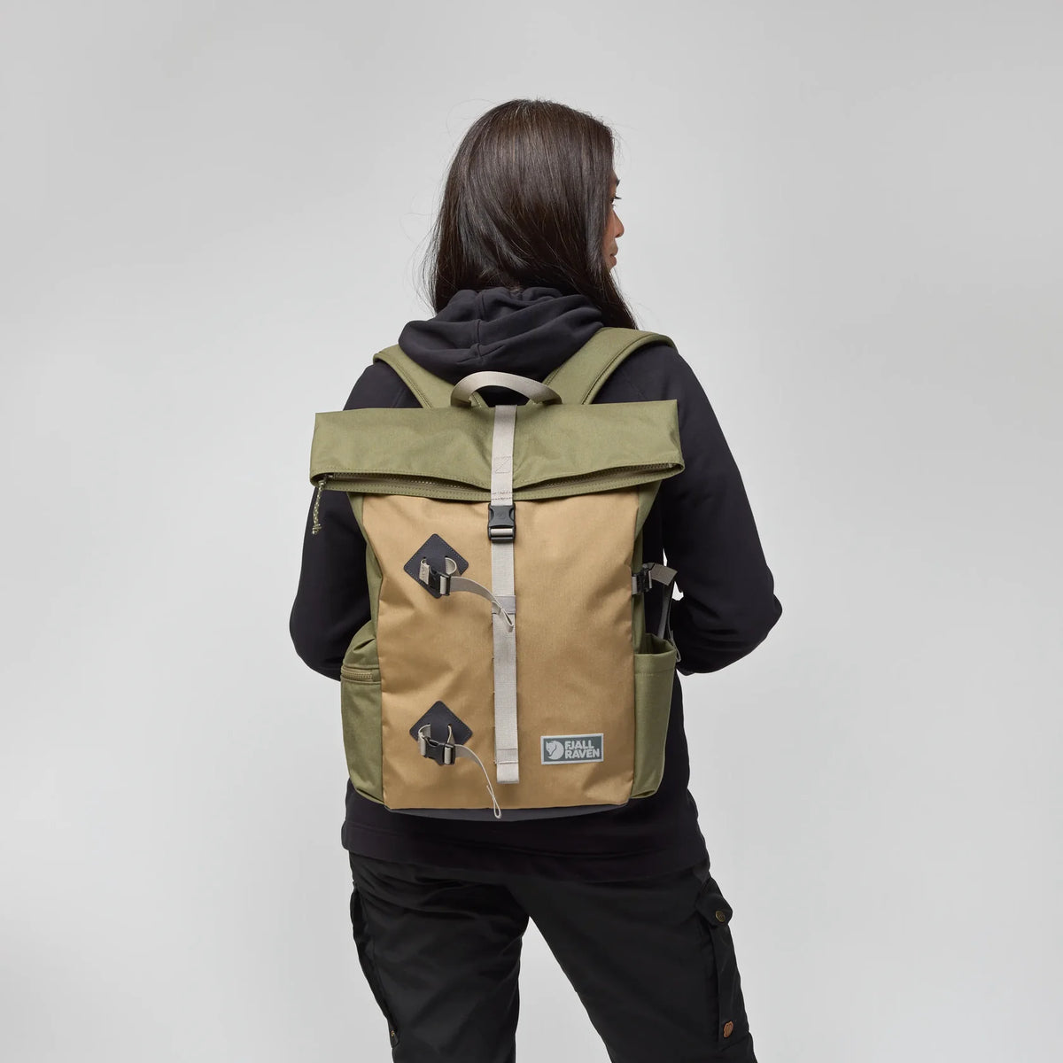 Person wearing a tan and green backpack on a plain background - Fjällräven Vardag Foldsack 25 - Green/Clay