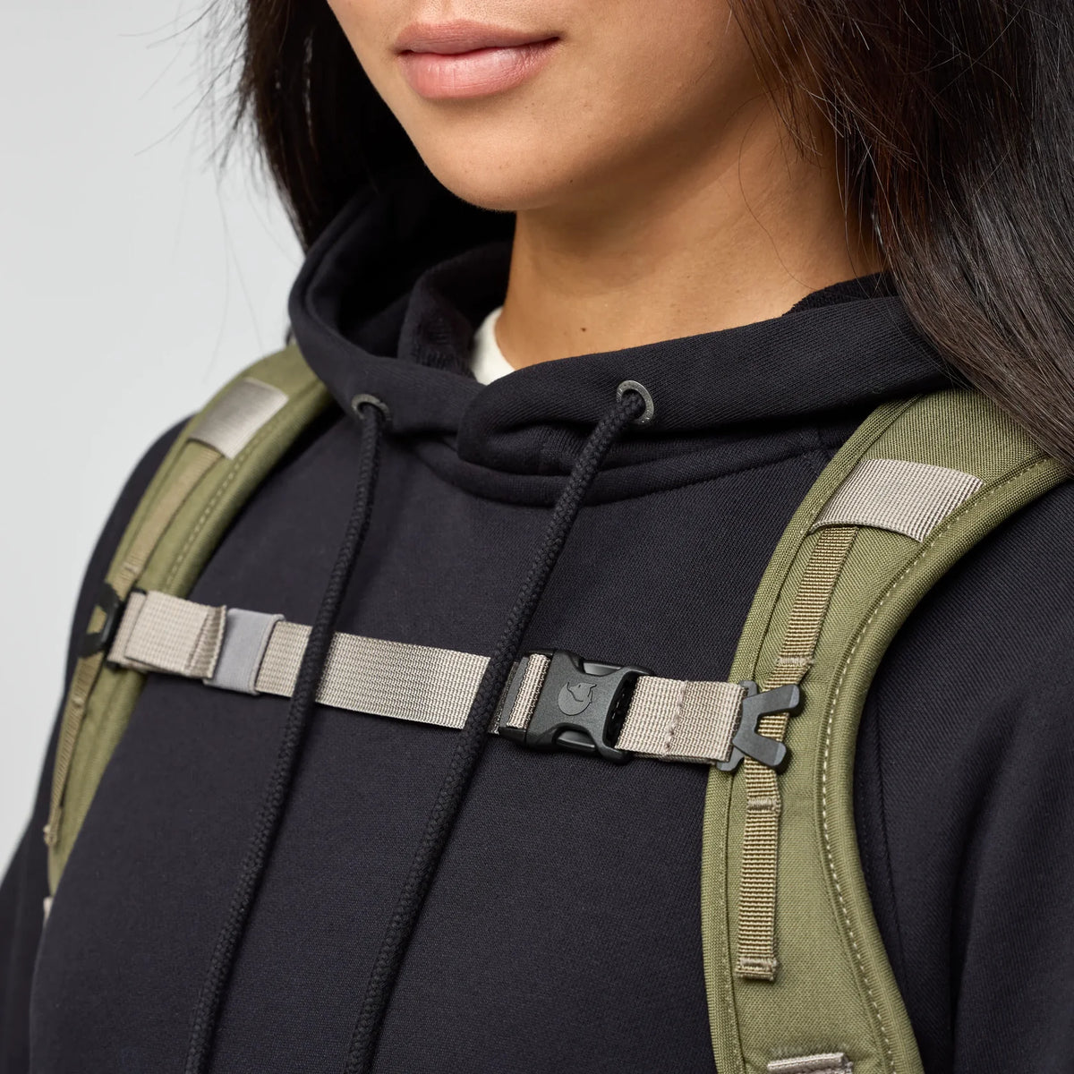 Person wearing a black hoodie with a green backpack on a light gray background - Fjällräven Vardag Foldsack 25 - Green/Clay