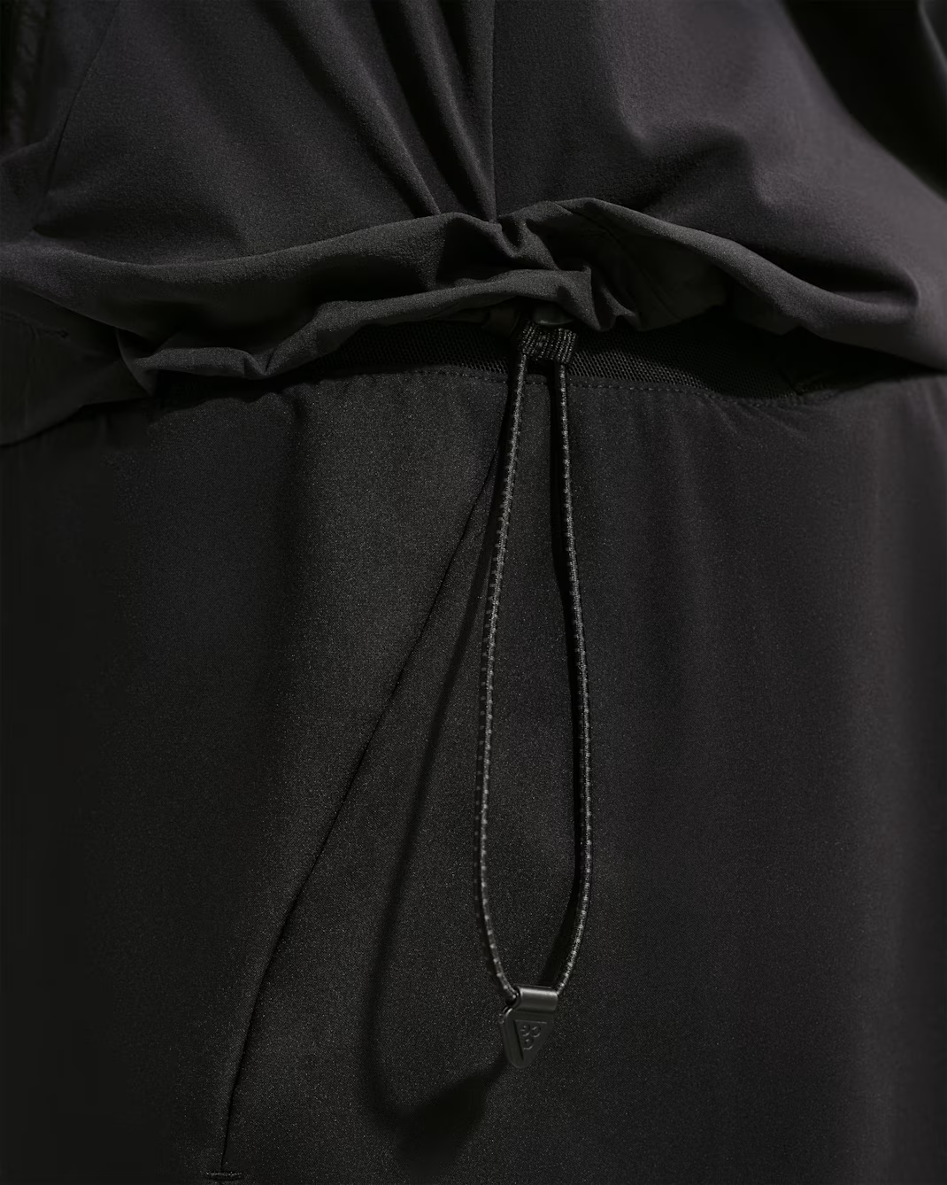 Close-up of a black draped garment with a gathered waist and a thin black drawstring hanging down, showing the fabric texture and stitching. - Nike ACG Lava Loft Therma-FIT Trail Running Jacket (Women's) - Black/Black/Black/Summit White