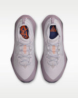 A Nike ACG ZEGAMA ZOOMX trail running shoe in a light lavender and purple colorway, featuring a textured mesh upper, a purple Swoosh, and a purple Vibram outsole, shown from a side profile on a light gray background.