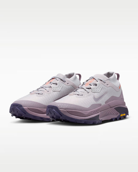 A Nike ACG ZEGAMA ZOOMX trail running shoe in a light lavender and purple colorway, featuring a textured mesh upper, a purple Swoosh, and a purple Vibram outsole, shown from a side profile on a light gray background.