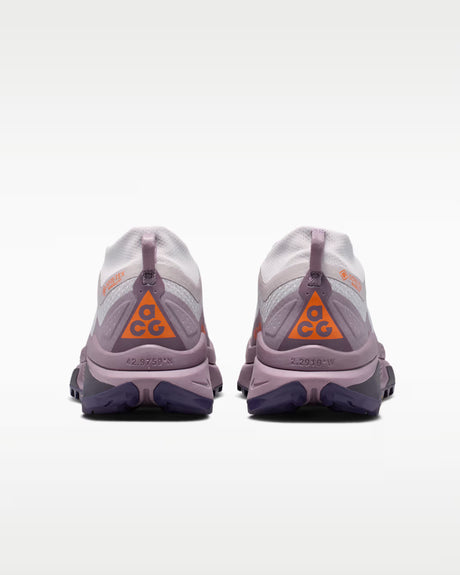A Nike ACG ZEGAMA ZOOMX trail running shoe in a light lavender and purple colorway, featuring a textured mesh upper, a purple Swoosh, and a purple Vibram outsole, shown from a side profile on a light gray background.
