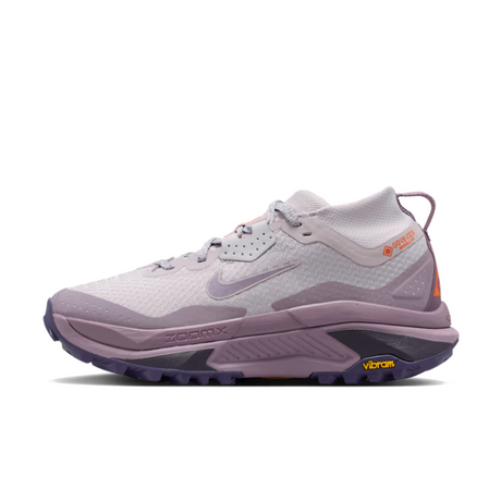 A Nike ACG ZEGAMA ZOOMX trail running shoe in a light lavender and purple colorway, featuring a textured mesh upper, a purple Swoosh, and a purple Vibram outsole, shown from a side profile on a light gray background.