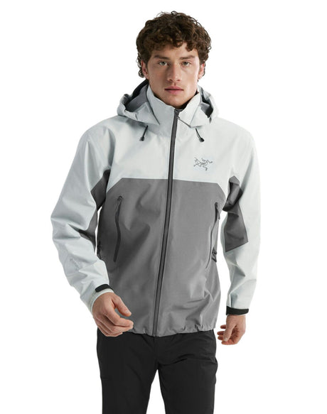 A man wearing a light gray and dark gray color-blocked Arc'teryx hooded jacket, paired with black pants, against a plain white background. - Arc'teryx Beta AR GORE-TEX Jacket (Men's) - Solitude/Void
