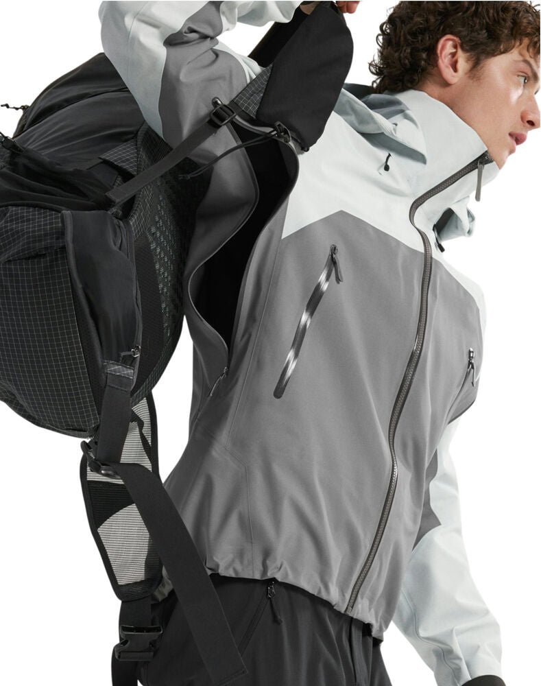 A close-up of a person wearing a gray and white technical outdoor jacket and carrying a black backpack, shown against a plain white background. - Arc'teryx Beta AR GORE-TEX Jacket (Men's) - Solitude/Void