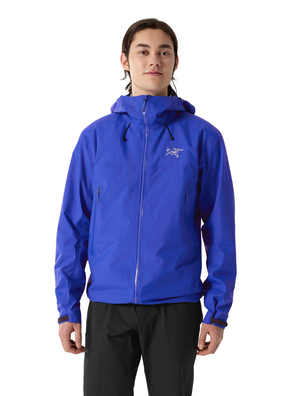 A man wearing a bright blue Arc'teryx hooded jacket with a full-zip front and black pants, standing against a plain white background. - Arc'teryx Beta SL GORE-TEX Jacket (Men's) - Vitality II