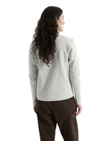 A woman with long, wavy dark hair is shown from the back wearing a light heather gray knit sweater and dark brown pants against a plain white background. - Arc'teryx Covert Cardigan (Women's) - Atmos Heather