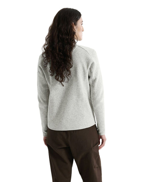 A woman with long, wavy dark hair is shown from the back wearing a light heather gray knit sweater and dark brown pants against a plain white background. - Arc'teryx Covert Cardigan (Women's) - Atmos Heather