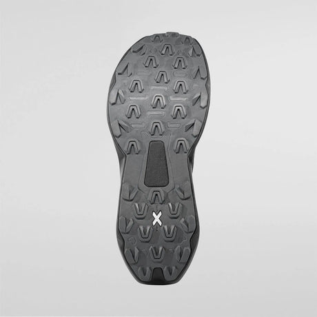 The outsole of a black athletic shoe, showing deep tread patterns and a small white stylized 'X' logo near the heel, photographed against a light gray background. - La Sportiva Prodigio 2 GORE-TEX Shoes (Women's) - Black/Reflective