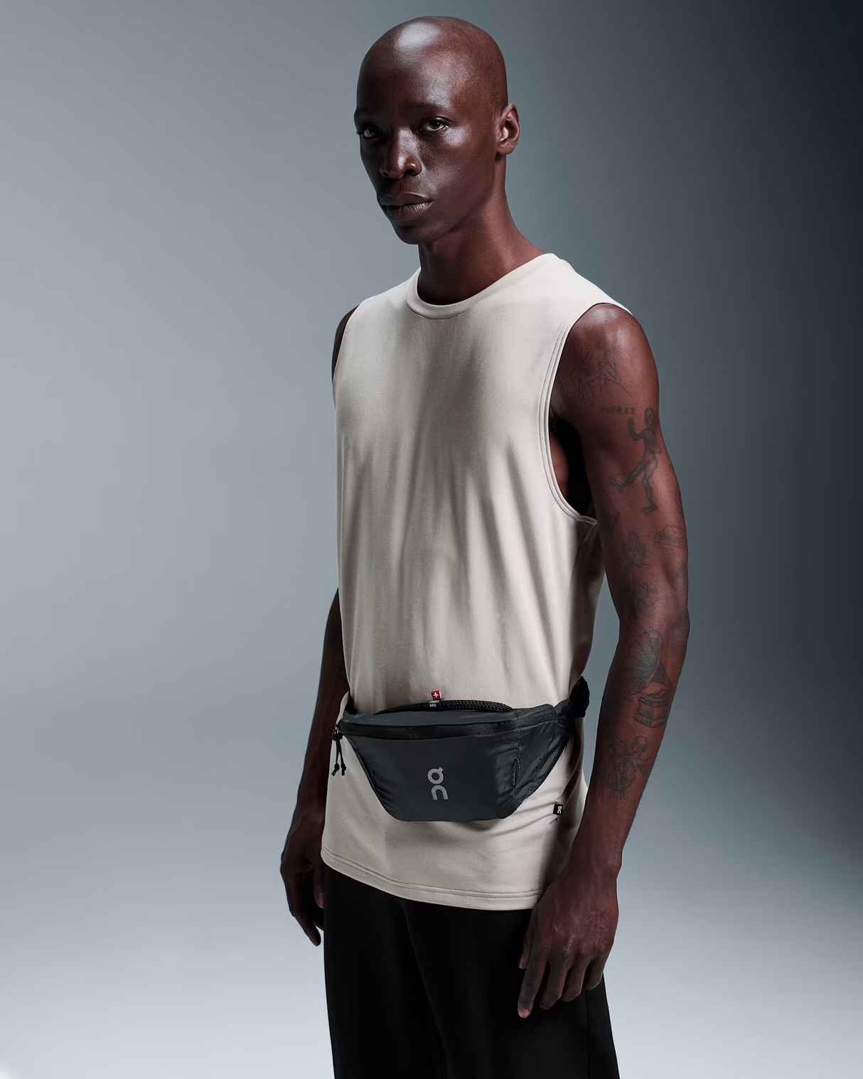 Man wearing a beige tank top and black pants with a waist bag on a gray background - On Waist Pack 2L Lite - Magnet