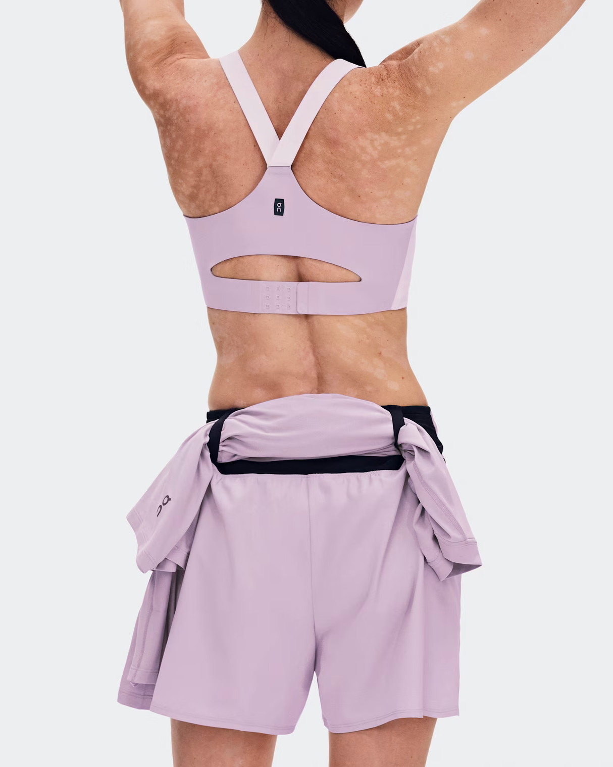 Rear view of a model wearing a light purple/lavender sports bra and matching shorts with a black waist tie belt, against a light gray studio background. - On Trail Shorts (Women's) - Foxglove