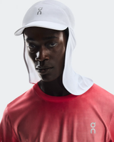 Person wearing a white cap and red shirt with a brand logo on a light gray background - On Solar Cap - White
