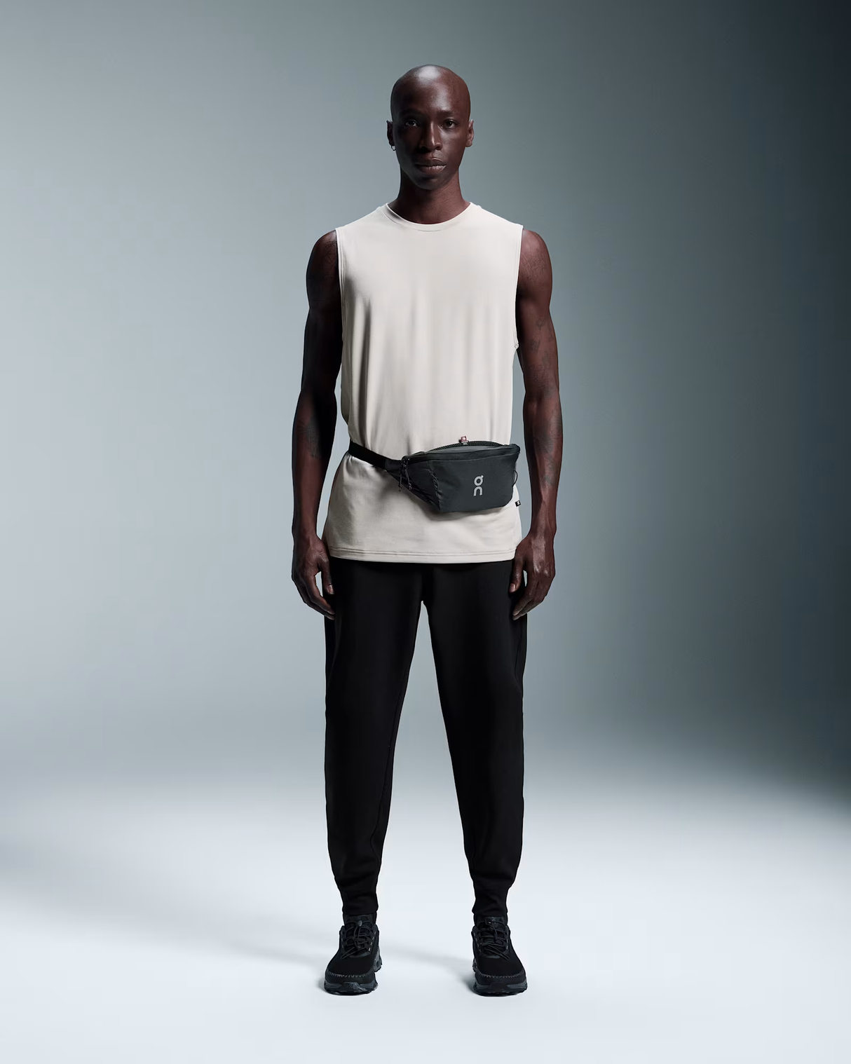 Man wearing a white sleeveless shirt and black pants with a fanny pack on a gray background - On Waist Pack 2L Lite - Magnet