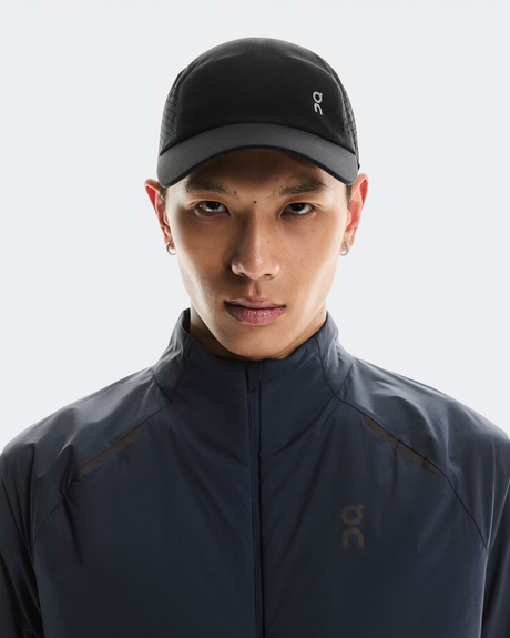 Person wearing a dark jacket and cap with a brand logo on a light gray background - On Lightweight Cap - Black