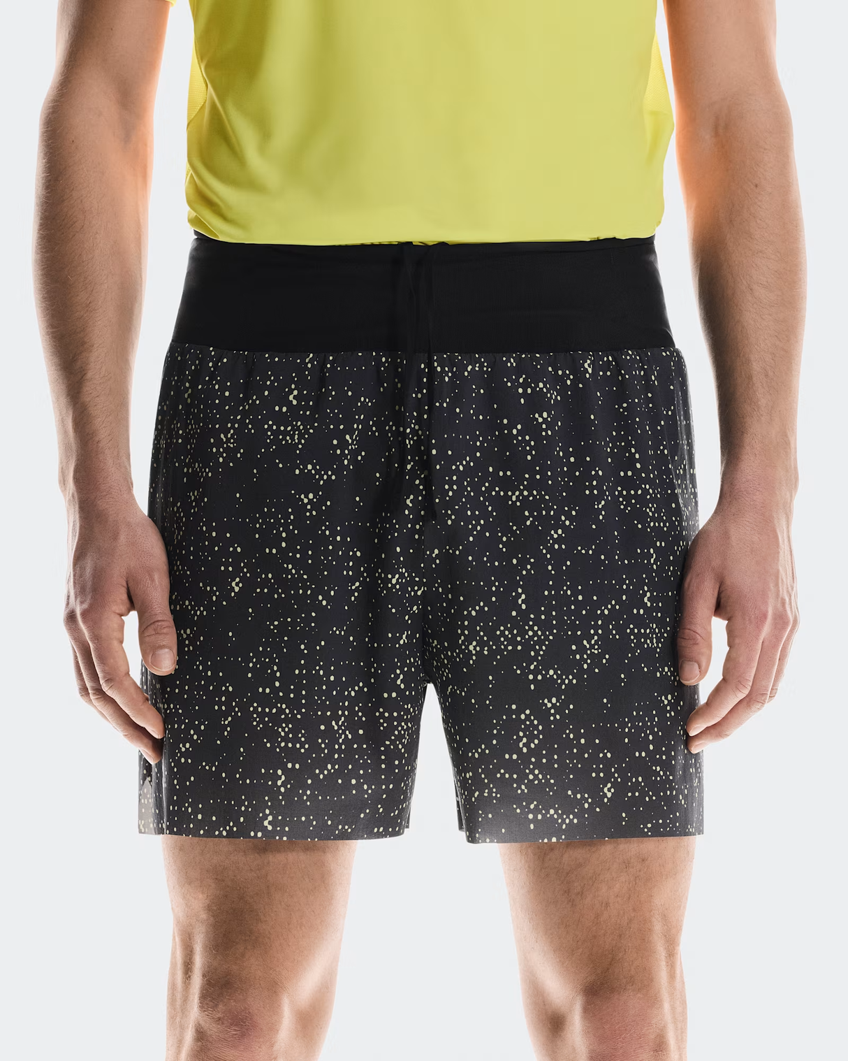 Person wearing black shorts with white speckle pattern and a yellow top on a light gray background - On Ultra Shorts (Men's) - Iron/Lime