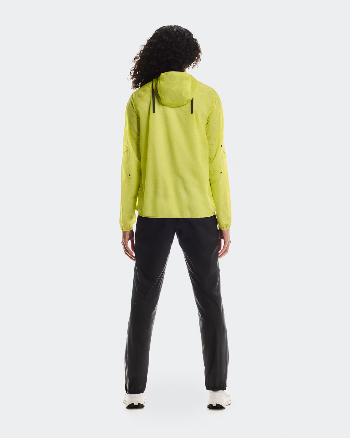 Person wearing a bright yellow raincoat and black pants on a white  - On Ultra Jacket (Women's) - Limelight/Limebackground