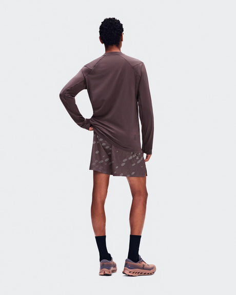 A model shown from the back wearing a brown long-sleeve athletic shirt and matching patterned shorts, paired with black socks and trail running shoes, against a light gray studio background. - On Trail Long-T Solar (Men's) - Mulberry
