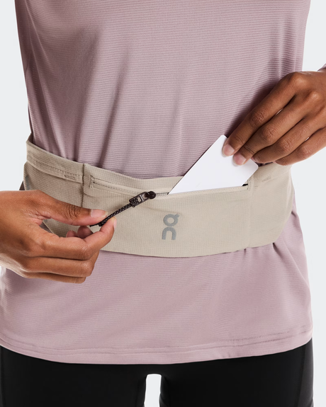 Person wearing a beige waist bag with a logo on a white background - On Speed Belt (Unisex) - Fog