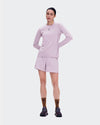 A woman modeling a light pink athletic long-sleeve top and matching shorts against a plain light gray studio background. - On Trail Shorts (Women's) - Foxglove