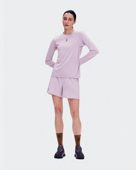 A woman modeling a light pink athletic long-sleeve top and matching shorts against a plain light gray studio background. - On Trail Shorts (Women's) - Foxglove