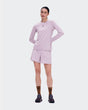 A woman modeling a light pink athletic long-sleeve top and matching shorts against a plain light gray studio background. - On Trail Shorts (Women's) - Foxglove