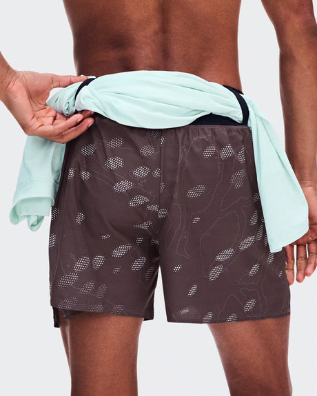 A close-up back view of a model wearing dark brown swim trunks with a white topographic pattern, with a mint green shirt tied around the waist. - On Trail Shorts (Men's) - Mulberry