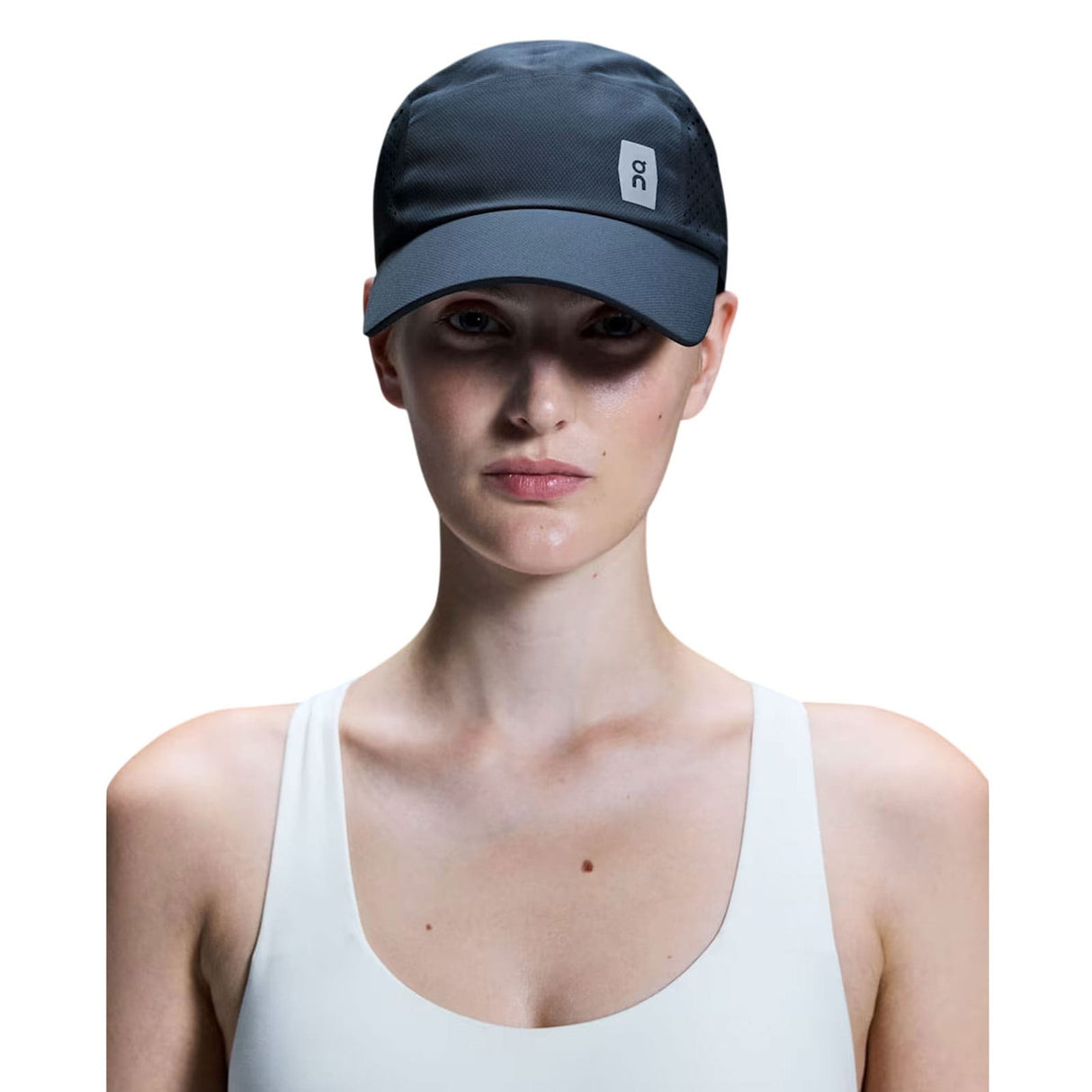 A model wearing a dark gray athletic cap with a small white square logo on the side, paired with a white tank top against a solid white background. - On Lightweight Cap - Navy