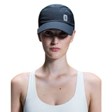A model wearing a dark gray athletic cap with a small white square logo on the side, paired with a white tank top against a solid white background. - On Lightweight Cap - Navy