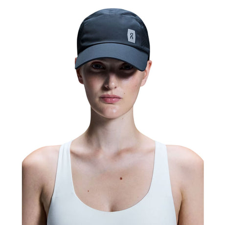 A model wearing a dark gray athletic cap with a small white square logo on the side, paired with a white tank top against a solid white background. - On Lightweight Cap - Navy