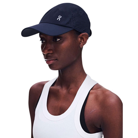 A woman wearing a dark navy athletic cap with a white 'on' logo, paired with a white tank top, shown against a plain white background. - On Lightweight Cap - Navy