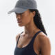 Woman wearing a gray cap with a brand logo on a white background - On Lightweight Cap - Rock