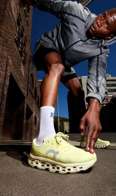 Person wearing bright yellow cloudmonster 3 running shoes with a blue sky and urban background