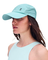 A woman in profile wearing a light mint green athletic cap with perforated back panels and a small black On logo, against a plain white background. - On Lightweight Cap - Wash