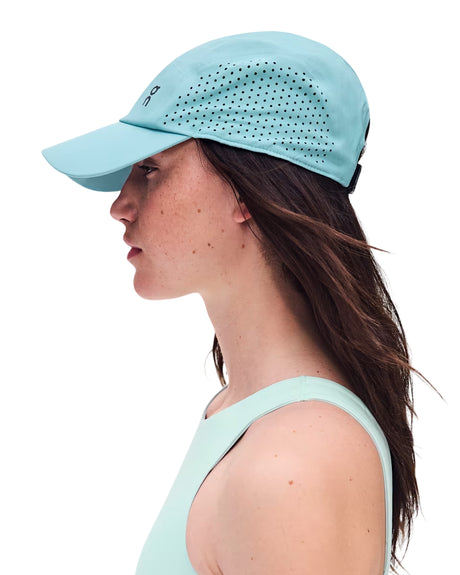 A woman in profile wearing a light blue athletic cap with perforated side panels and a matching light blue sleeveless top, photographed against a plain white background. - On Lightweight Cap - Wash