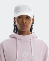 Person wearing a light pink hoodie and white cap with a logo on a white background - On Lightweight Cap - White