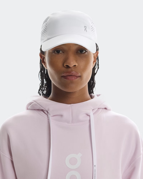 Person wearing a light pink hoodie and white cap with a logo on a white background - On Lightweight Cap - White