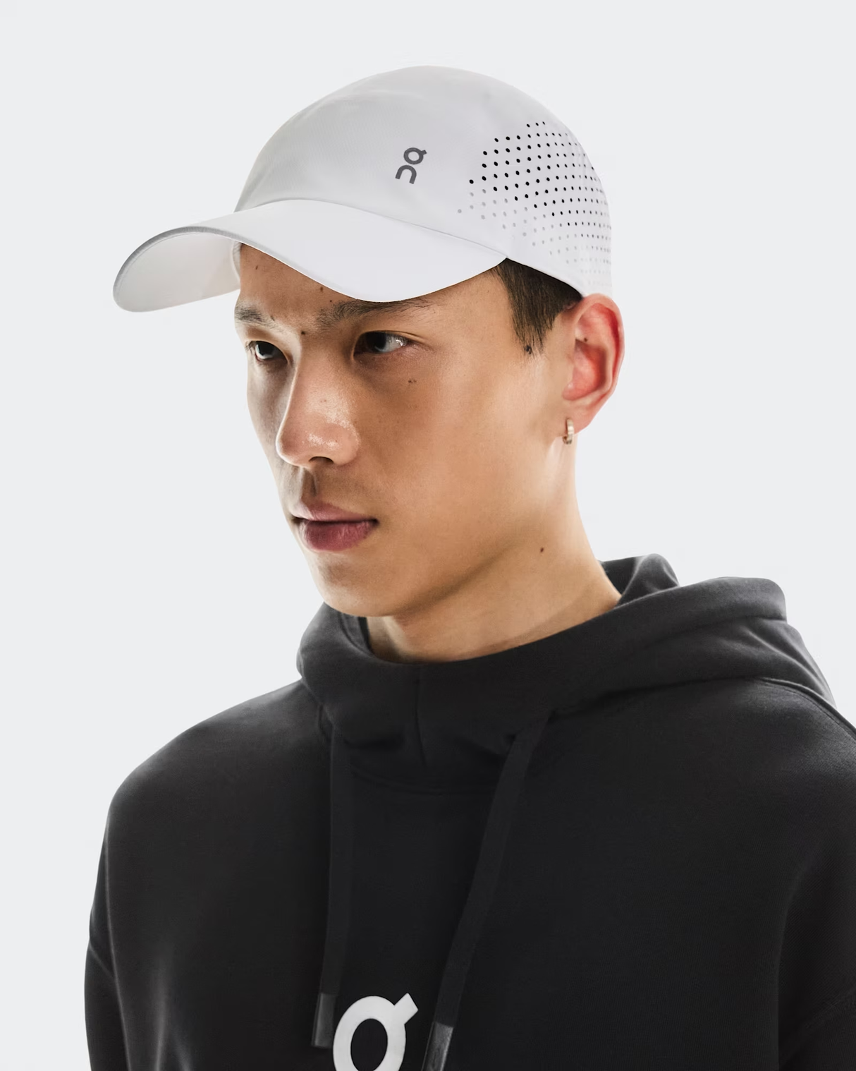 Person wearing a black hoodie and white cap with a logo on a light gray background - On Lightweight Cap - White